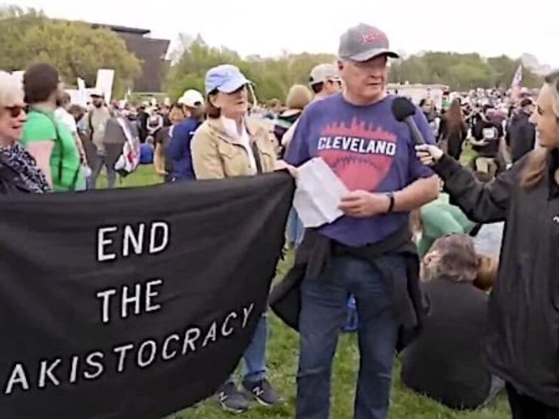 An Elon Musk protester has to read from a piece of paper what the sign he is holding means during a 'Hands Off!' rally on Saturday, April 5, 2025 (Video screenshot)
