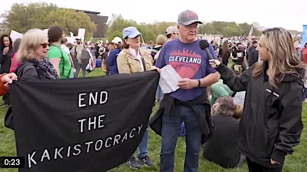 An Elon Musk protester has to read from a piece of paper what the sign he is holding means during a 'Hands Off!' rally on Saturday, April 5, 2025 (Video screenshot)